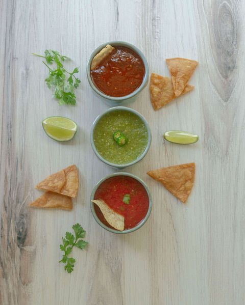Three bowls of Mexican salsas arranged vertically with tortilla chips, lime wedges, and cilantro: tomato salsa (mild), green salsa (medium), and red salsa (spicy).
