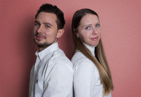 Two people stand with their backs to each other and look straight ahead.