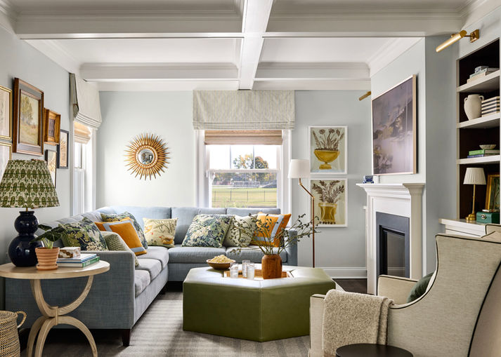 A living room with colorful artwork on the walls, a light blue sectional sofa and a green ottoman. 