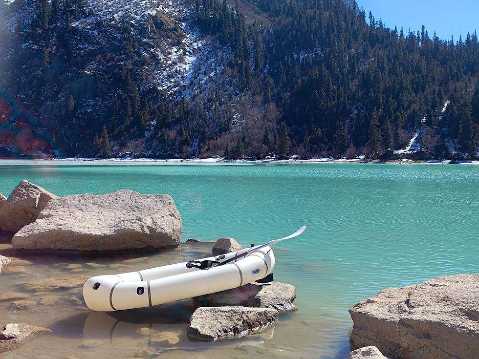 An inflatable packraft pulled up on the rocky shore of a turquoise alpine lake