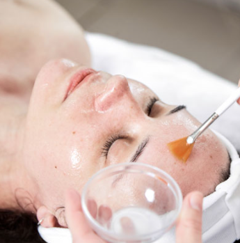 Nahaufnahme eines Mannes, der eine Green Peel Fresh Up Behandlung erhält. Auf seiner Wange ist eine goldene Kräutermaske aufgetragen, die einen Teil seines Bartes bedeckt. Er hat dunkle Haare und einen gepflegten Bart und schaut mit einem leichten Lächeln direkt in die Kamera. Der Hintergrund ist hellgrau und neutral. Die Behandlung zielt darauf ab, die Haut durch die Anwendung einer natürlichen Kräutermischung zu erfrischen und zu revitalisieren.  Die Green Peel Fresh Up Behandlung ist eine sanfte Methode der Kräuterschälkur, die die Haut nicht schält, sondern mit natürlichen Kräutern anregt und erfrischt. Sie basiert auf einer Mischung aus ausgewählten Kräutern, Algen, Mineralien und Enzymen, die in die Haut einmassiert werden. Die Behandlung stimuliert die Durchblutung, öffnet die Poren und bereitet die Haut optimal auf die Aufnahme von Wirkstoffen aus anschließenden Pflegeprodukten vor.  Die Vorteile der Green Peel Fresh Up Behandlung sind:  Sofortiger Frische-Kick: Die Behandlung 