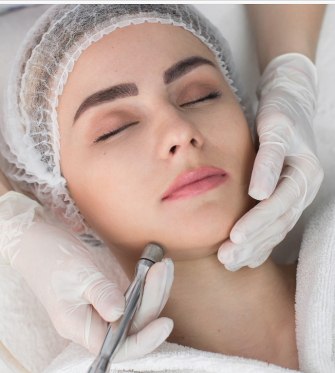 Nahaufnahme eines Mannes, der eine Green Peel Fresh Up Behandlung erhält. Auf seiner Wange ist eine goldene Kräutermaske aufgetragen, die einen Teil seines Bartes bedeckt. Er hat dunkle Haare und einen gepflegten Bart und schaut mit einem leichten Lächeln direkt in die Kamera. Der Hintergrund ist hellgrau und neutral. Die Behandlung zielt darauf ab, die Haut durch die Anwendung einer natürlichen Kräutermischung zu erfrischen und zu revitalisieren.  Die Green Peel Fresh Up Behandlung ist eine sanfte Methode der Kräuterschälkur, die die Haut nicht schält, sondern mit natürlichen Kräutern anregt und erfrischt. Sie basiert auf einer Mischung aus ausgewählten Kräutern, Algen, Mineralien und Enzymen, die in die Haut einmassiert werden. Die Behandlung stimuliert die Durchblutung, öffnet die Poren und bereitet die Haut optimal auf die Aufnahme von Wirkstoffen aus anschließenden Pflegeprodukten vor.  Die Vorteile der Green Peel Fresh Up Behandlung sind:  Sofortiger Frische-Kick: Die Behandlung 