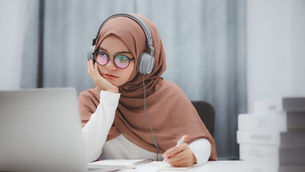 A young woman sits at her laptop with headphones engaged in a business English training course.