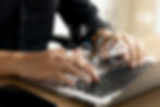 Hands typing on a laptop with digital cloud icons and data symbols overlay, suggesting a tech or cloud computing theme in a modern setting.