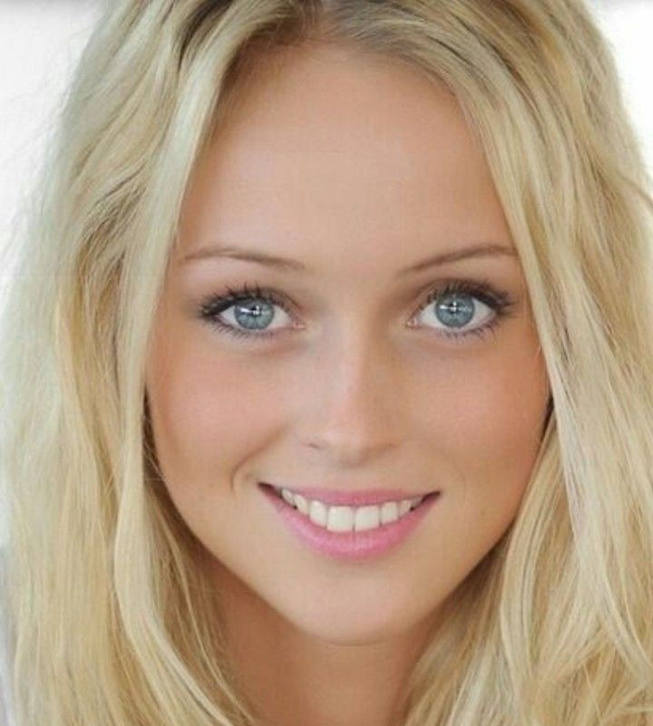 A person with long blonde hair and blue eyes smiles warmly at the camera.