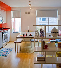 Bright kitchen and dining area with white furniture, colorful decor accents, and open shelving, feat