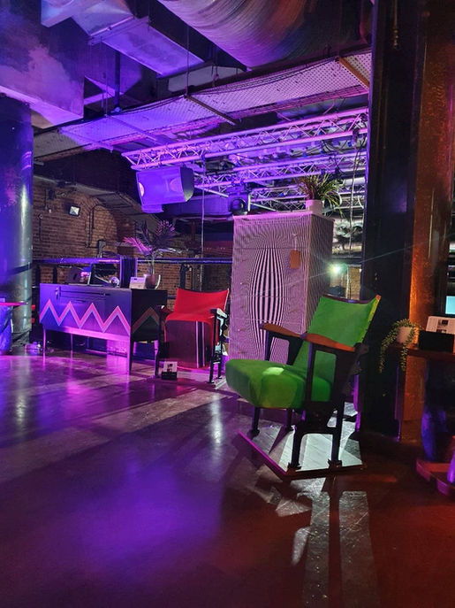 Green and red cinema seata, a black and white chest of drawers and black sideboard set as a trade stand in a dimly lit nightclub environment.