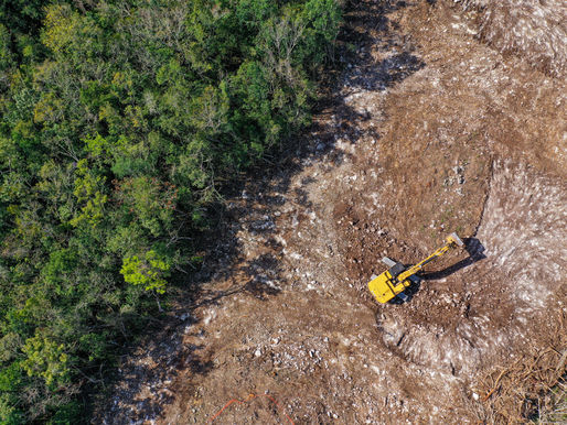 Vue aérienne de la déforestation avec une excavatrice défrichant des terres, illustrant les émissions non vérifiées dans les chaînes d’approvisionnement et la nécessité de données précises sur la déforestation pour atteindre les objectifs Net Zéro. – Koltiva.com