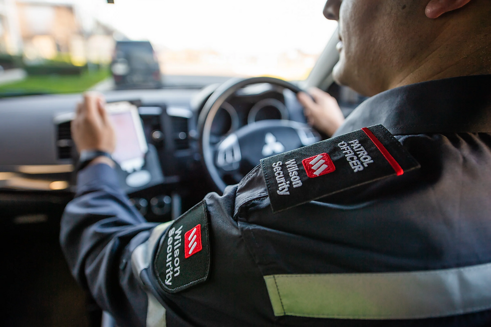 Wilson Security officer in uniform monitoring operations from vehicle, demonstrating the integrated security solutions within Wilson Group's multi-business portfolio that relies on optimised cloud resource management through Cloud Ctrl.