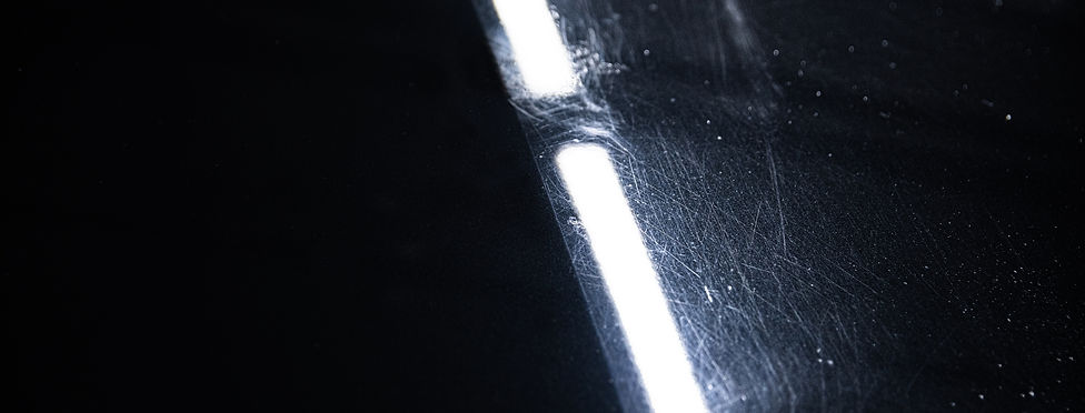 "Close-up view of a black car's surface under bright inspection lights, showing a clear contrast between a polished and an un