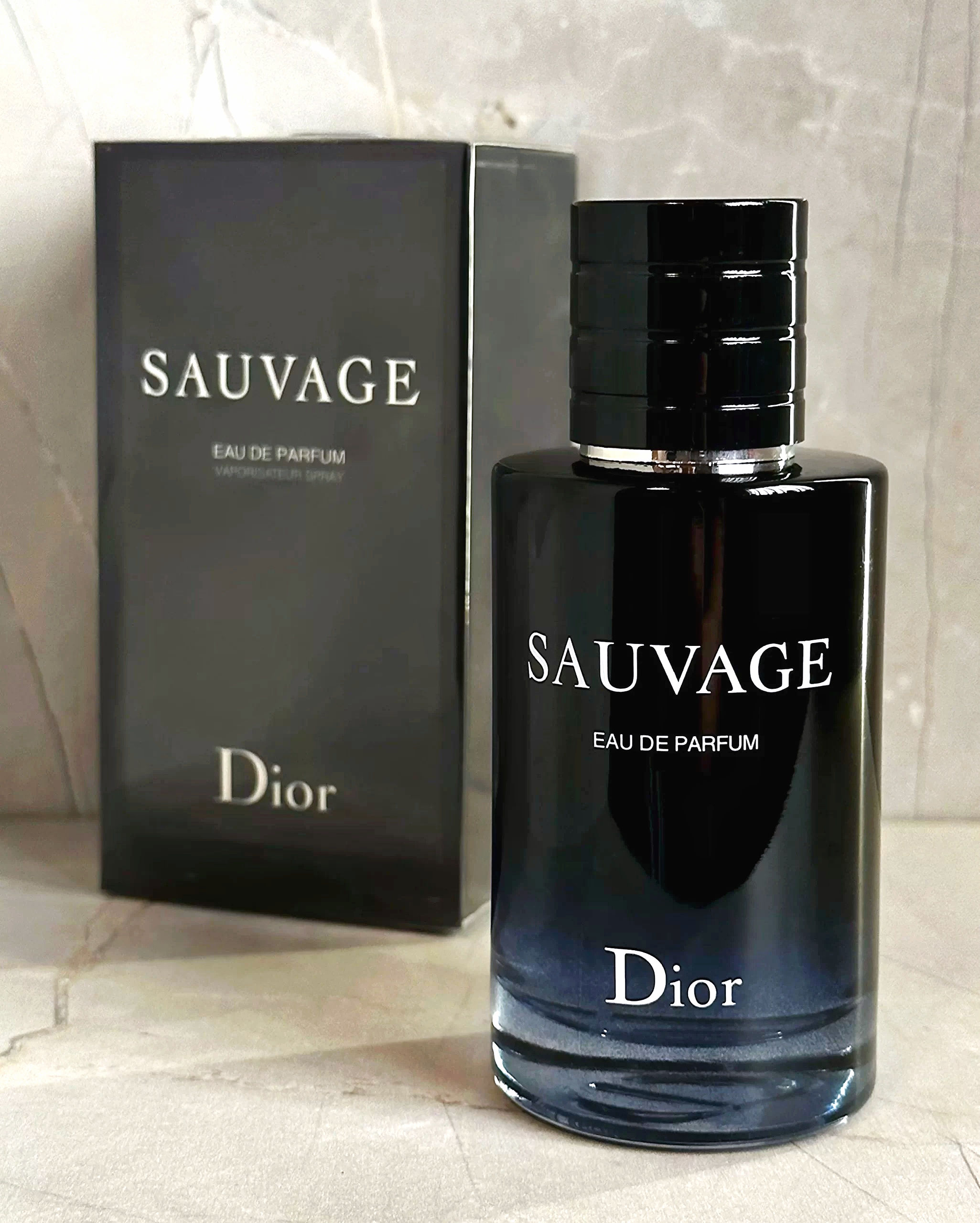Vista frontal frasco perfume Sauvage Dior de 100ml junto a su caja en fondo marmol