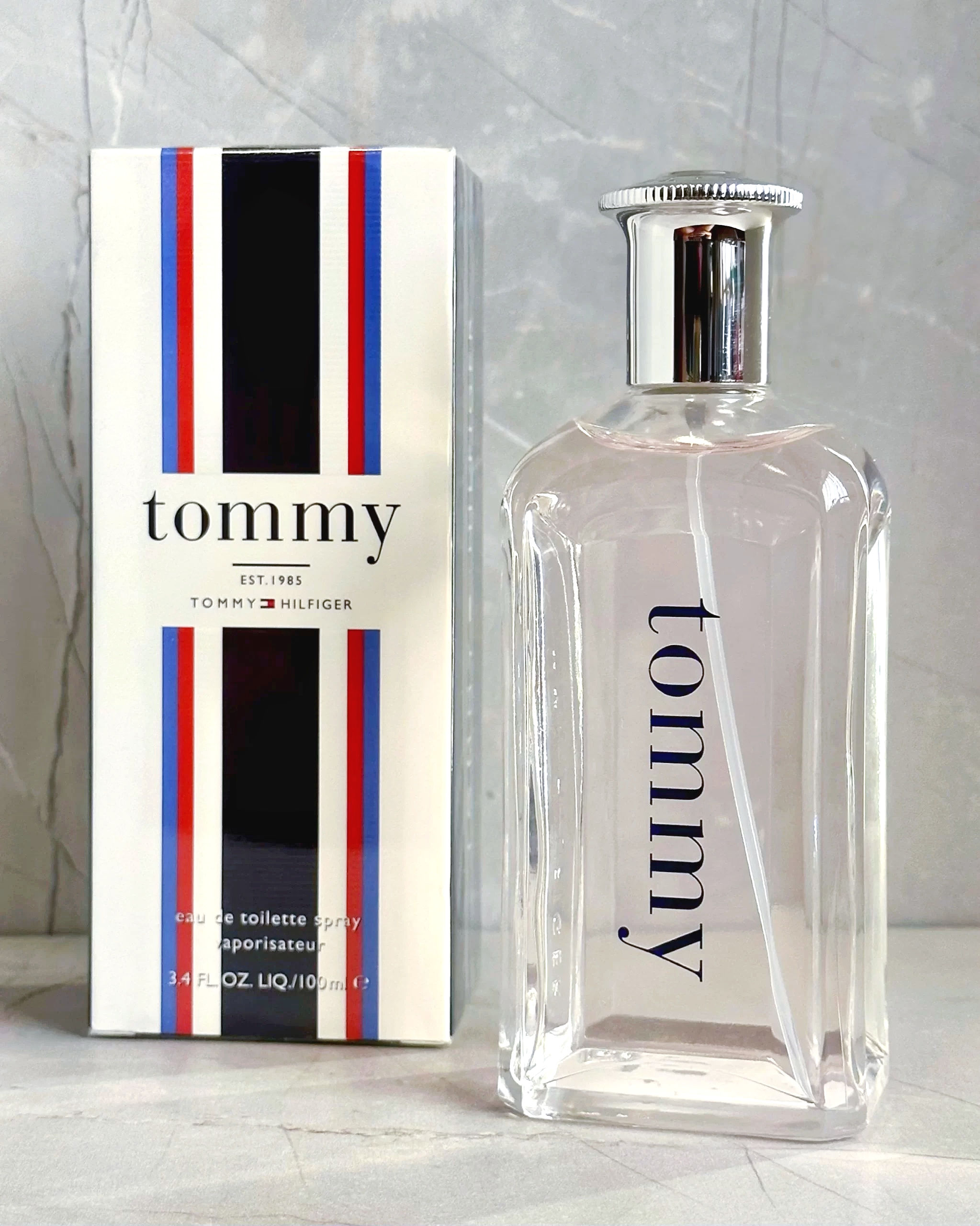 Vista frontal frasco perfume Tommy de 100ml junto a su caja en fondo marmol