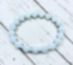 Handcrafted aquamarine beaded bracelet in soft pale blue photographed on white wood plank surface.
