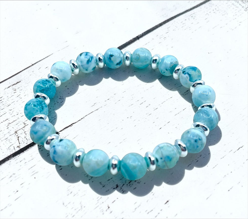 Handcrafted matte blue agate beaded bracelet photographed on white wood plank surface.