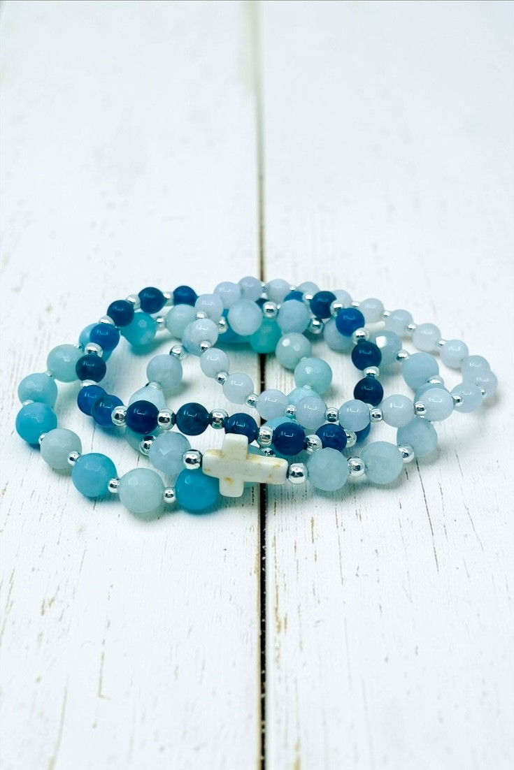 Coastal Faith bracelet stack with aquamarine, apatite, and amazonite beads and white jade arranged on white wood background w