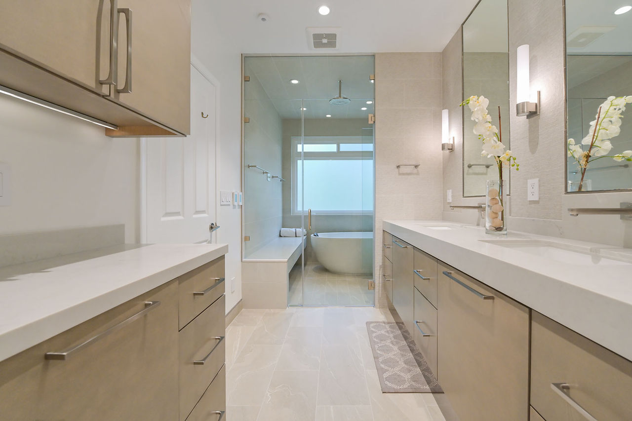 Contemporary bathroom with double vanities, neutral cabinetry, and a glass-enclosed wetroom featuring a soaking tub.