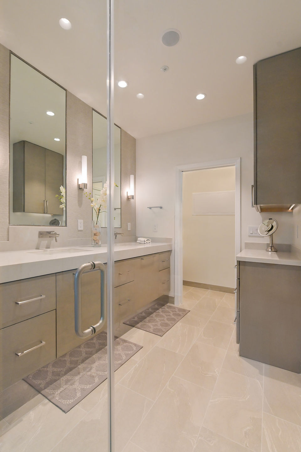 Contemporary bathroom with double vanities, large mirrors, modern lighting, and neutral cabinetry.