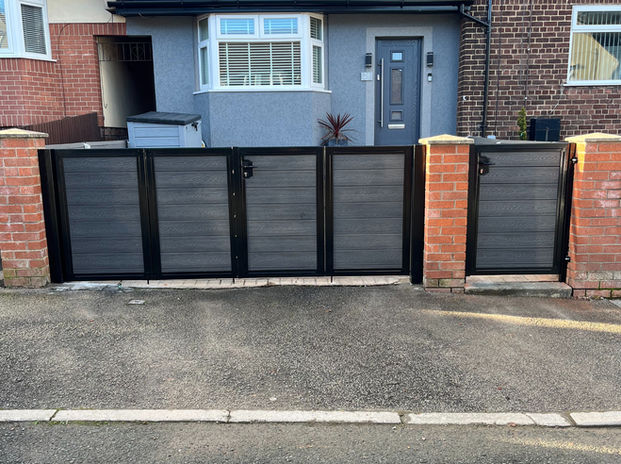 Set of bifold gates with four panels, featuring a black outer frame and anthracite composite wood infills; a matching pedestrian gate on the right, in the same design