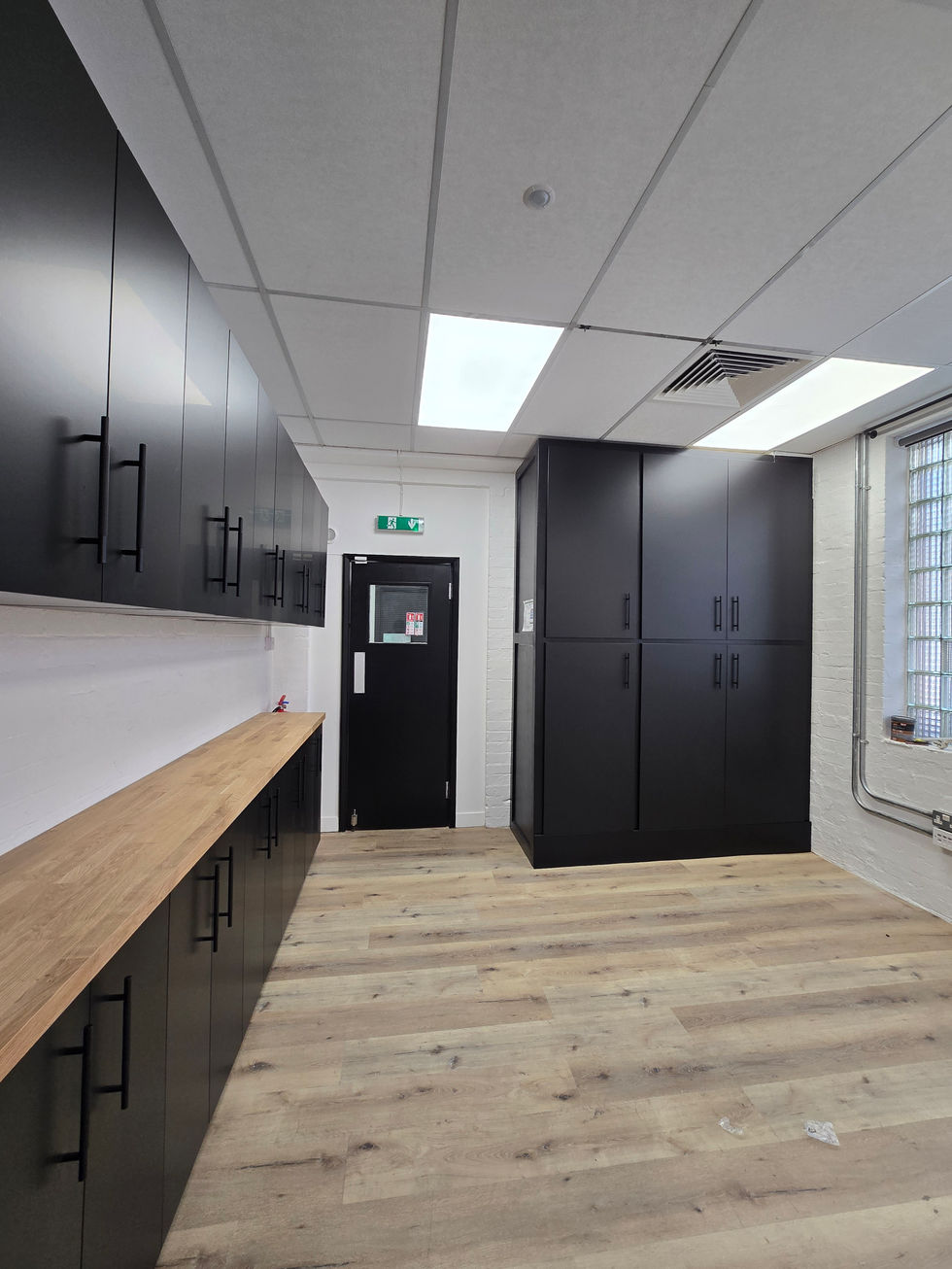 Completed built‑in office cupboard wall featuring black lower cabinets, matching black upper cupboards, and a wooden countertop