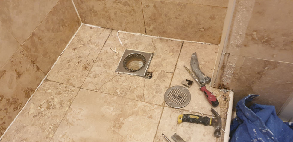 Shower floor with the drain exposed and tools laid out while tiles are prepared for repair and re‑tiling.