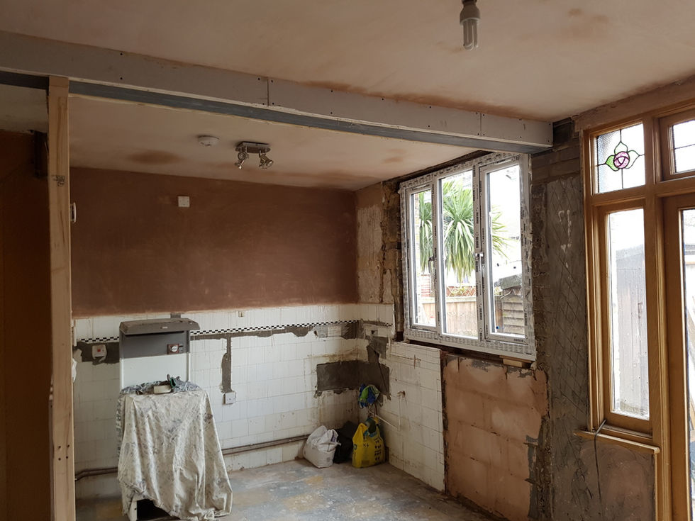 Kitchen renovation in the preparation stage with exposed plaster, unfinished walls, and construction materials on the floor.