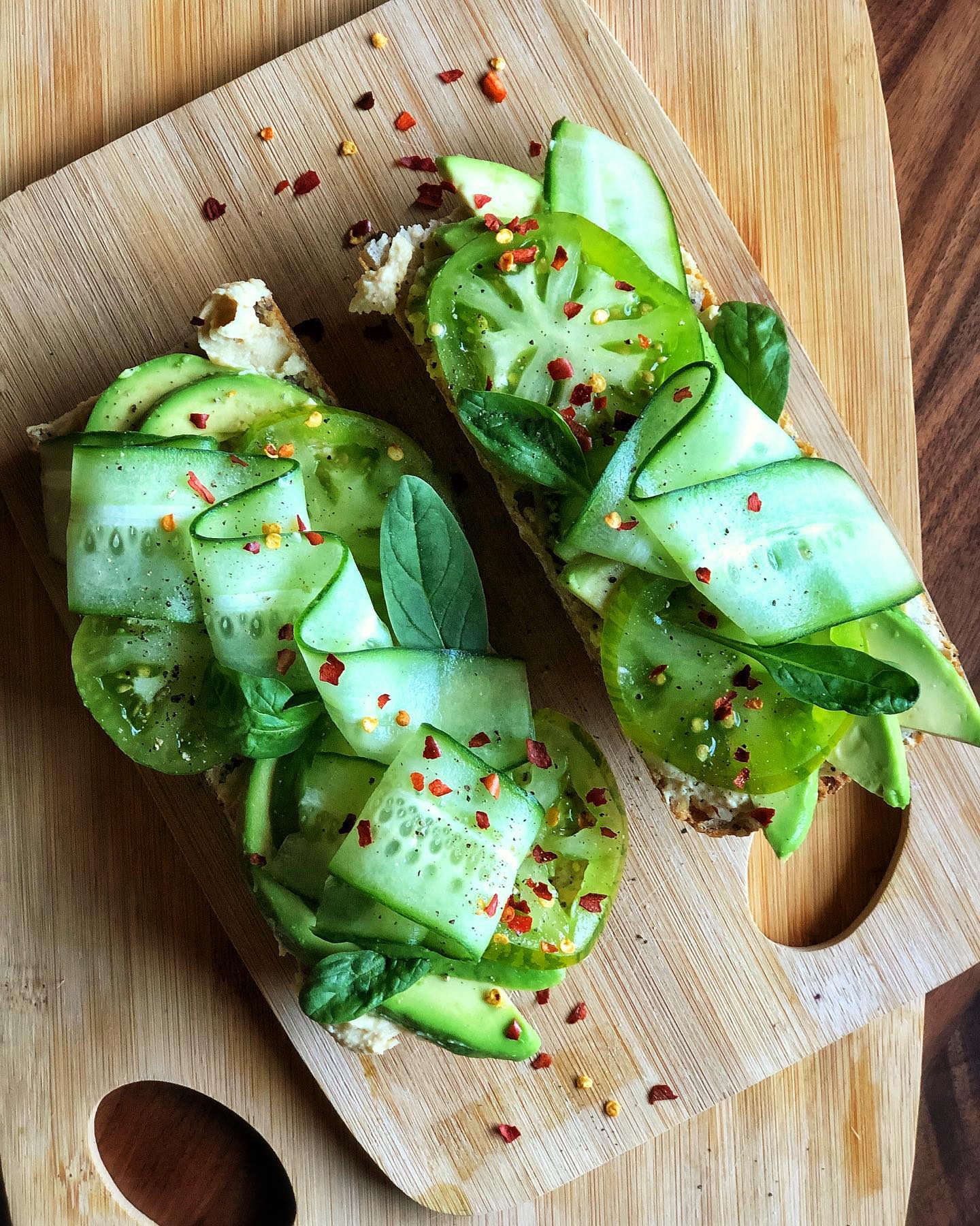 Avocado toast with heirloom tomato, cucumber ribbons, spinach, hummus, and chili flakes