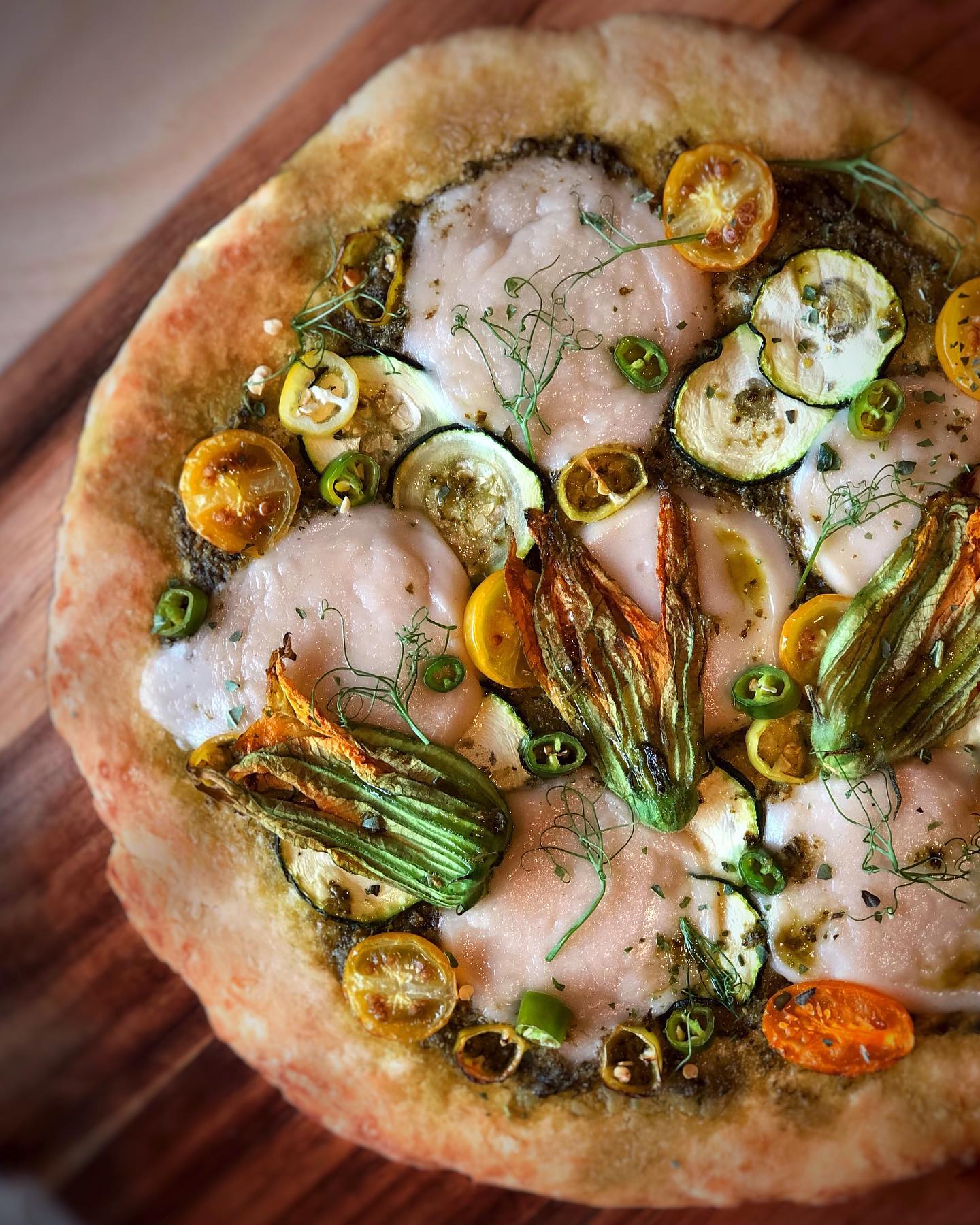 Rustic vegan zucchini blossom pizza with pesto, tomatoes, jalapeños, and mozzarella