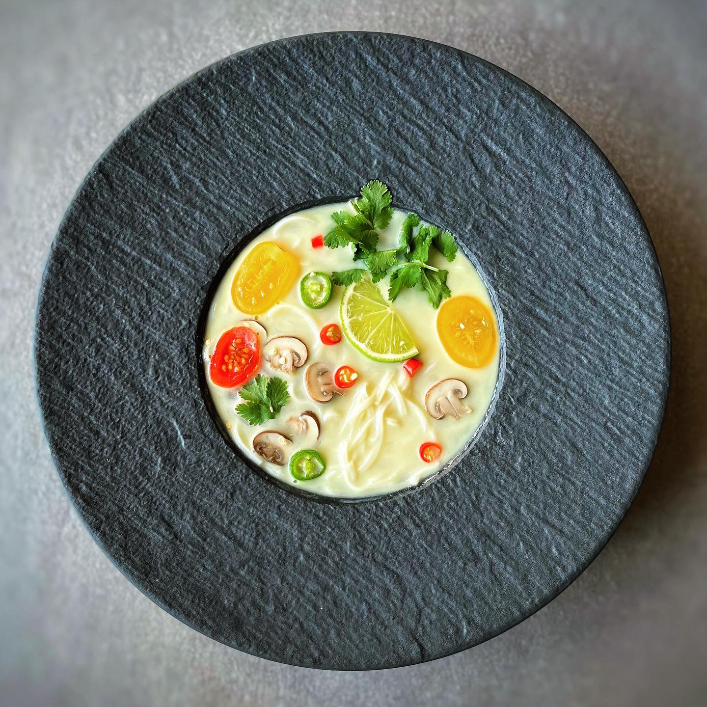 Vegan Tom Kha soup with rice noodles, coconut milk, mushrooms, tomatoes, lime, and cilantro