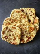 Homemade vegan naan breads with golden brown bubbles stacked on a plate