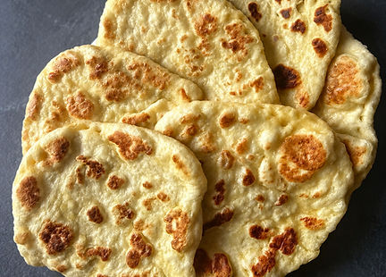 Homemade vegan naan breads with golden brown bubbles stacked on a plate