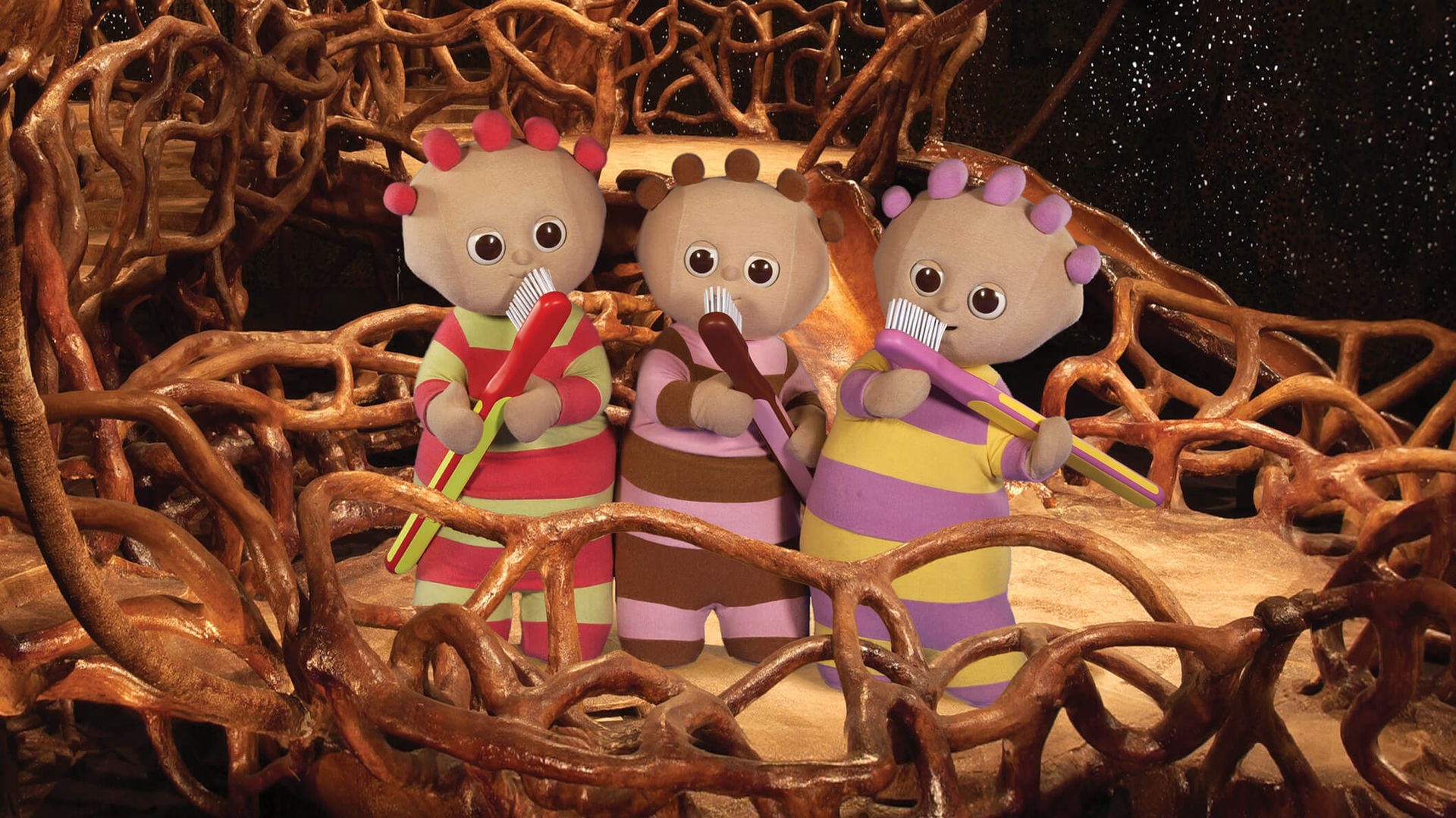 Three cute characters, wearing striped pyjama, are standing inside a wicker basket and holding large toothbrushes close to their face. 