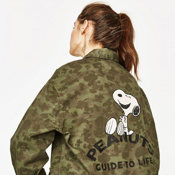 A close-up of a woman’s back wearing an army green jacket. In the middle of the jacket is an image of a black and white dog and text that says Snoopy Guide to Life.