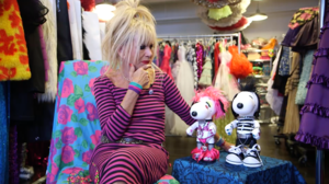 blond woman in a pink dress next to two dog figures wearing punk rock clothing