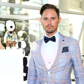 man in a blue and red plaid suit stands next to 2 dog statues wearing white and rose dress and suit