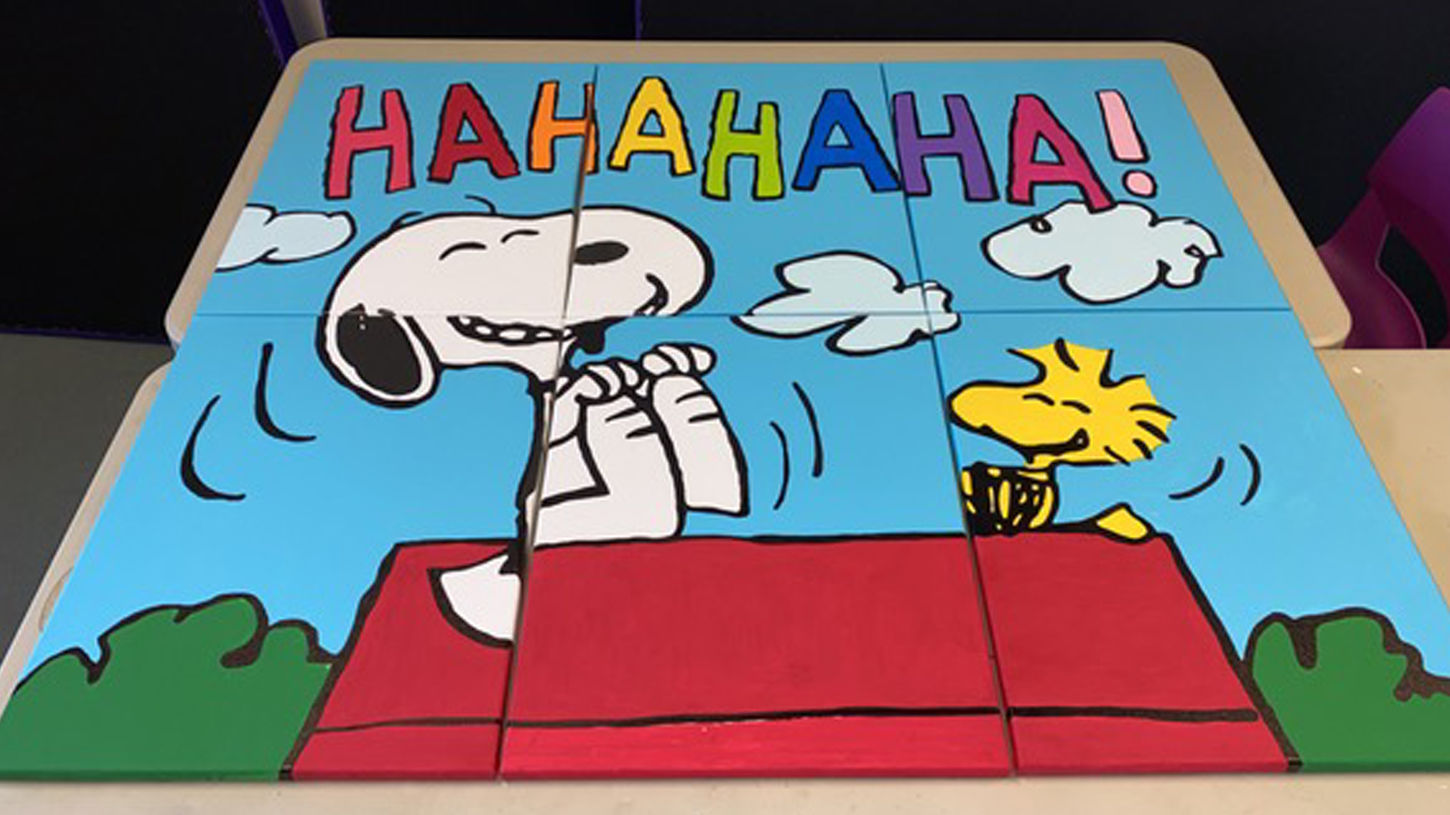 A painted mural of a black and white beagle and yellow bird laughing.