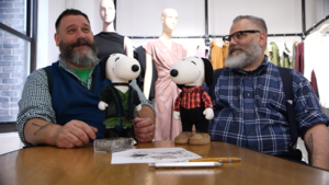 two bearded men ith two dog figures. one in a jacketand one in a plaid shirt