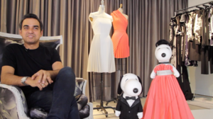 a man sits next to two dog figures. one in a tuxedo and one in a long pink dress