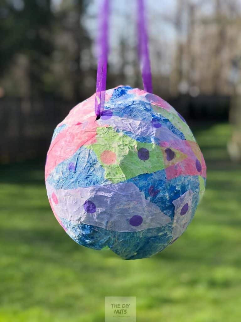 A homemade, multicoloured, paper mache pinata, hung off purple ribbon.