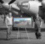 russ proctor and tony agar standing next to a framed oil painting with the actual mosquito ww2 fighter in the background