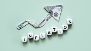 Folded U.S. dollar bills form an upward arrow above letter blocks spelling “inflation” on a pale green background.