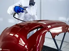 Un peintre carrossier applique une couche de peinture sur un pare choc