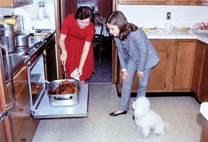 Preparing the turkey for the Garland Family dinner in 1964. Rose Garland is checking the turkey while her daughter and pet poodle look on.