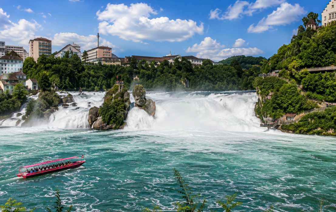 Der Rheinfall in der Schweiz mit gewaltigen Wassermassen, Aussichtspunkten und einem Boot auf dem türkisfarbenen Wasser bei sonnigem Wetter.