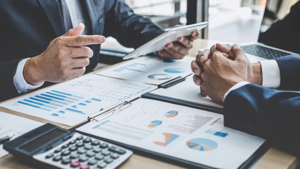 homens sentamos a mesa com papeis e calculadora enquanto avaliam de é possível fazer redução de custos.