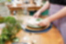 Close nas mãos de Amandha Silveira, enquanto prepara uma mesa de jantar, seguindo a melhor etiqueta de Mesa Posta, para a organização dos utensílios.