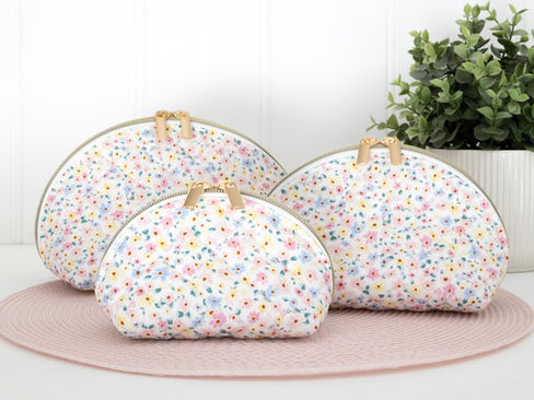 A set of three clam shaped zip pouches sitting on a pink mat on a table.