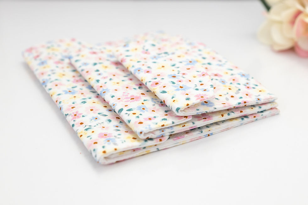 Folded pastel floral pouches stacked on a white surface, with a soft blurred flower in the top right.