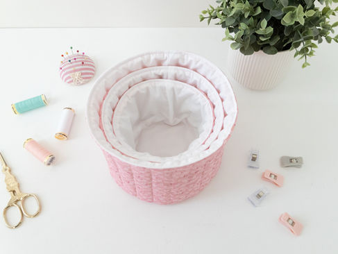 A set of three pink and white quilted round baskets nested inside one another and sitting on a table.
