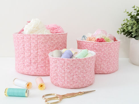 A set of three pink and white round quilted baskets filled with craft supplies and sitting on a table.