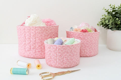A set of three pink quilted baskets filled with sewing supplies.